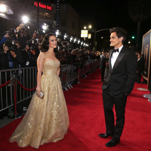 Katy Perry and John Mayer at the Hollywood premiere of a major film. Katy in a stunning golden, floor-length gown. John in a classic black tuxedo. Red carpet scene, paparazzi flash