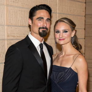 Kevin Richardson and Kristin Kay Willits at a gala event. Kevin, with goatee and dark hair, and Kristin with makeup, stand against a textured wall backdrop.