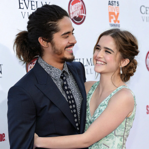 Avan Jogia and Zoey Deutch at a Hollywood premiere. Both in formal attire. Embrace with warm smiles. White backdrop with promotional logos
