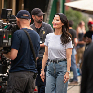 Lucy Liu on the set of a new film. Wearing casual attire, jeans and a t-shirt. Surrounded by crew members and filmmakers.