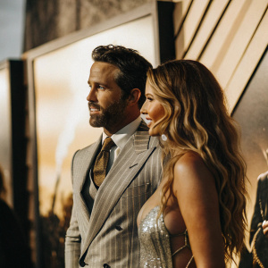 Ryan Reynolds and Blake Lively at movie premiere. He is in a gray pinstripe suit with a beard. She is in a shimmering dress with a loose updo. Gradient and graphic elements form the backdrop.