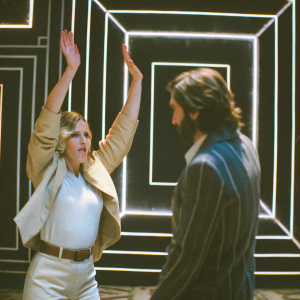 Scarlett Johansson and Jake Gyllenhaal at an awards show. Geometric patterned backdrop. Scarlett raises her arms, Jake makes gestures.