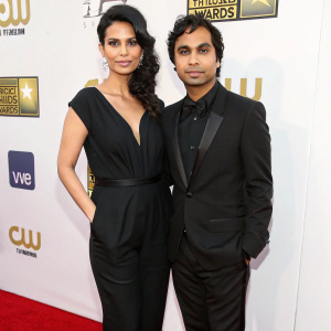 Neha Kapur and Kunal Nayyar, both adorned in formal attire, on the carpet of the Critics' Choice Awards. Neha in a sophisticated black jumpsuit, Kunal in a stylish black suit, the background is simple white with minimal logos