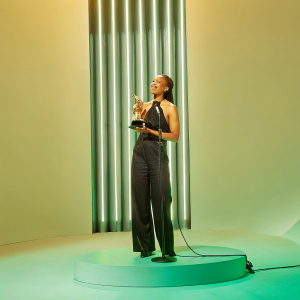 Esperanza Spalding, receiving a statue at the Grammy Awards. Black attire, standing on stage.