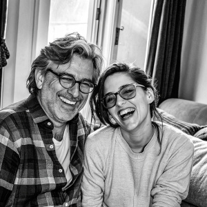 Griffin Dunne and Kristen Stewart sharing a laugh indoors. Casual attire, smiling for the camera.