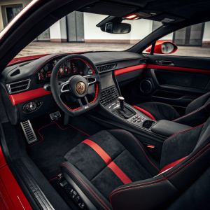 Inside a sleek red Porsche 911 GT3 RS. Dark interior, black seats contrasting with red accents. Driver sits in black leather seat.