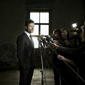 Xabi Alonso, dressed in a sleek black suit, at the post-match press conference. A sea of microphones and cameras in the background.