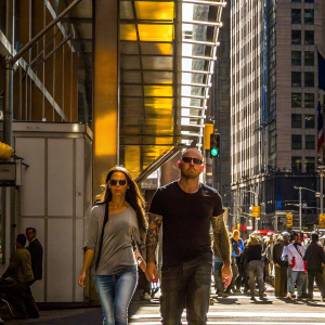Megan Fox and Brian Austin Green walking down a busy city street. Megan Fox wearing oversized sunglasses and casual jeans. Brian Austin Green's arms are visible with tattoos. Crowded urban backdrop.