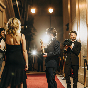 Kristen Stewart, Rick Carter, and Daniel Radcliffe at a glitzy Hollywood awards ceremony. Carter receives a prestigious golden statuette.