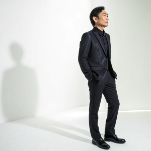Dicky Cheung in a sleek black suit, standing solo in a bright studio setting. Solemn expression