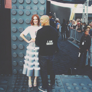 Vin Diesel and Karen Gillan at a Lego movie premiere. Vin Diesel, bald head, wearing black shirt with 'I AM SROOT' logo. Karen Gillan, red hair, in white top and flowy skirt. Crowded outdoor venue with Lego-themed backdrop.