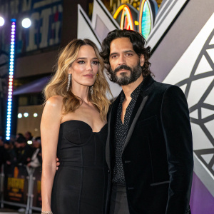 Laura Chiatti and Marco Bocci attend Italian premiere of 'Black Panther: Wakanda Forever'. Laura in black dress, Marco in dark velvet blazer. Background features geometric shapes and vibrant lights.