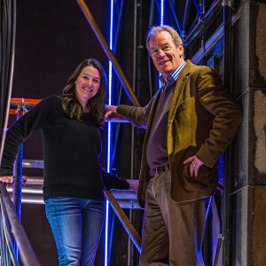Caucasian actors Nichole Kessler and John C. McGinley at a gala event. Kessler in black sweater and jeans, McGinley in brown jacket and shirt. Dark backdrop