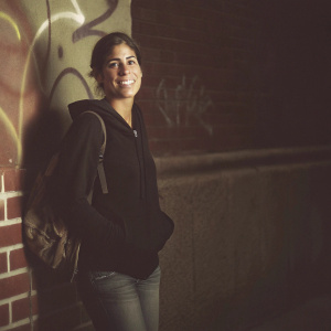 Ana Ortiz, known for her role as Hilda in 'Ugly Betty,' captured in an urban setting. Dressed casually in a black hoodie and jeans. Graffiti-covered brick wall backdrop