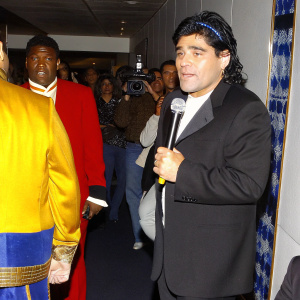 Diego Maradona at a press conference, holding a microphone. Crowd in background