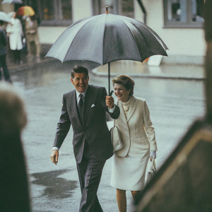 Ronald and Nancy Reagan, dressed in formal attire, walking in the rain under an umbrella. A vintage black and white photo