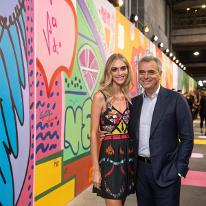 Chiara Ferragni and Ricardo Guadalupe at a fashion event. They are posing in front of a bright, colorful wall covered in graffiti.