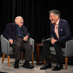 Don Rickles and Craig Ferguson laughing together. Onset of a late-night talk show. Black backdrop