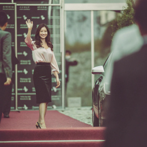 Shin Se-Gyeong at a high-profile watch launch event. She is wearing a chic pink blouse and black skirt, waving for the camera in front of a sleek Guess Watch branded backdrop.