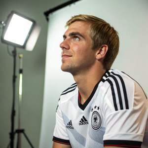 Philipp Lahm in a candid studio shot. Athletic build, blonde hair, calm demeanor. Wearing a white soccer jersey with black accents. Simple, light background. Studio lights highlighting his face and jersey.