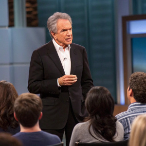 Warren Beatty in an intense discussion. Dark suit and white shirt. Studio audience watching