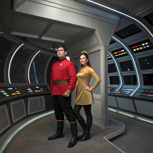A couple dressed in vintage Star Trek costumes standing in an empty, futuristic set with glowing control panels.