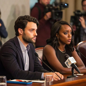 Jack Falahee and Aja Naomi King at a press conference. Both looking serious while sitting at a conference table.