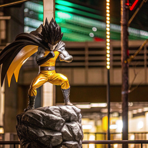 3D model of Saitama, from One Punch Man, mid-fight stance, standing on rock pedestal. Soft green and yellow gradient background