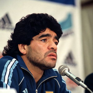 Diego Maradona in a candid shot during a press conference. Looking intense with his trademark nose. Clean-cut, no background distractions.
