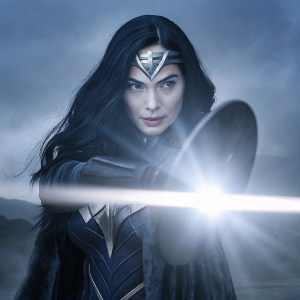 Gal Gadot as Wonder Woman, standing resolute with a glowing aura in front of a misty, sepia-toned backdrop. Her long, dark hair cascades over her shoulders. Intense gaze.