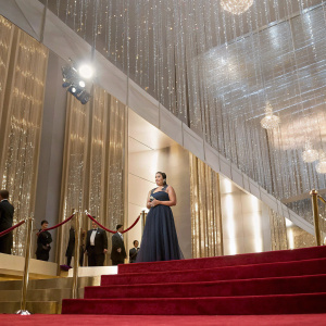 Gina Rodriguez accepting award at star-studded gala. Glittering chandelier, red carpet backdrop.