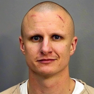 Jared Lee Loughner, in a mugshot. Bald head, pale skin, slight injuries visible. Straightforward gaze, detailed facial features. Neutral lighting, plain background