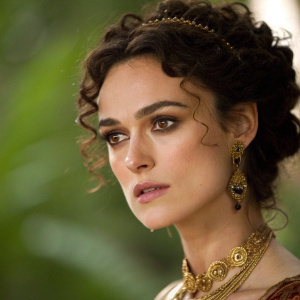 Close-up of Keira Knightley as Anna Karenina, elegant makeup, intense gaze, elaborate gold jewelry, dark curls, blurred green background.