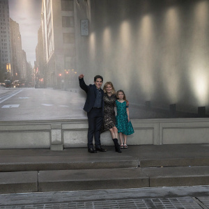 Ben Stiller and family at the Groundhog Day Broadway Opening. Christine Taylor in black floral dress, Ella Olivia Stiller in teal lace dress. Posed against a busy cityscape backdrop, soft natural light, candid poses