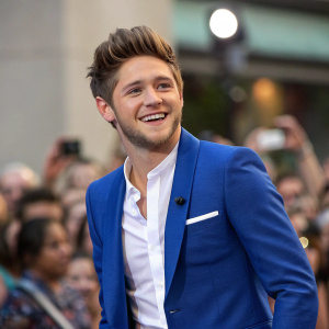 Niall Horan, singer, wearing a blue blazer and white shirt, smiling at camera. Crowd blurred in background.