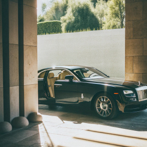 A stunning black Rolls-Royce Wraith parked outdoors. Its sleek design and matte finish stand out against the sunny backdrop.