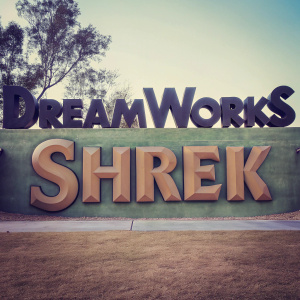 Whimsical cartoon-style DreamWorks logo with Shrek elements. Bright green backdrop. Bold, playful font and whimsical cartoonish details.