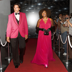Anthony Quinn and Jolanda Addolori in color, walking the red carpet of a glamorous Hollywood film festival. Wearing vintage attire, with a backdrop of twinkling lights and enthusiastic fans.