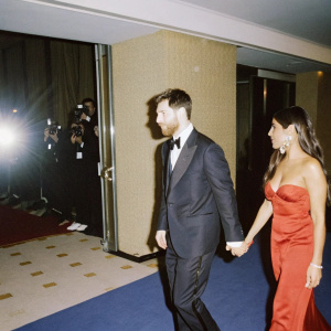Lionel Messi and Antonella Roccuzzo at a glitzy awards ceremony. Red carpet lined with flashing cameras. Elegant backdrop with shimmering logo displays.