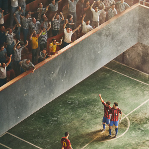 Marc Bartra, in Barcelona FC jersey, celebrating a goal with teammates. Green field, spectators in the background.