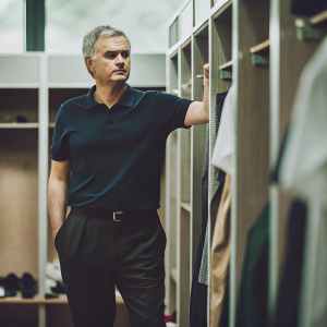 Jose Mourinho, standing in the locker room. Intense facial expression, wearing a navy blue polo shirt and black dress pants.