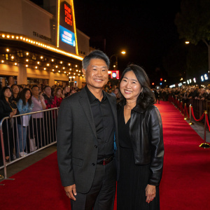 John Tso and Nancy Tso at the AMC Burbank 16 film festival premiere. They are standing on a red carpet with flashing lights and crowds of fans.