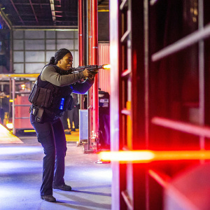 Regina King as FBI Agent Simone Clark. Dressed in tactical gear, aiming a gun. Dimly lit indoor training facility.