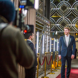 Joe Alwyn, dressed in a dark blue suit and white shirt, smiles for the cameras. Golden Globe Awards ceremony. Luxurious red carpet backdrop