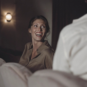 Shannon Elizabeth, in a brown blouse, smiling broadly at a film festival. Dark background with soft lighting. Candid close-up photo.