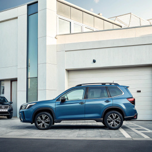 Blue Subaru Forester SUV parked in front of a sleek urban garage. Clean, modern design with white walls in the background. Focused on the car's body and wheels