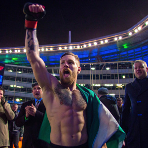 High-resolution shot of Conor McGregor shirtless, with his signature tattoos. Celebrating with a clenched fist, amidst a cheering crowd. Bright stadium lights, people clapping, and branded backdrop.