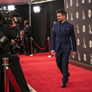 Juanes, the celebrated Colombian singer, arrives at the Grammy Awards ceremony. He is impeccably dressed in a navy suit and carries himself with star power.