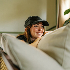 Caucasian woman Alexis Randock in a casual setting. Wearing a black baseball cap. Soft lighting highlights her face. Brown hair, warm smile
