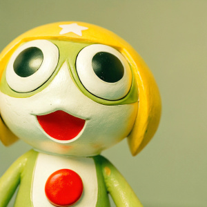 Close-up of the Keroro Gunso Kururu figure from the anime Sgt. Frog. Yellow and white coloring, large expressive eyes, red dot on chest, wide smile, stationary pose